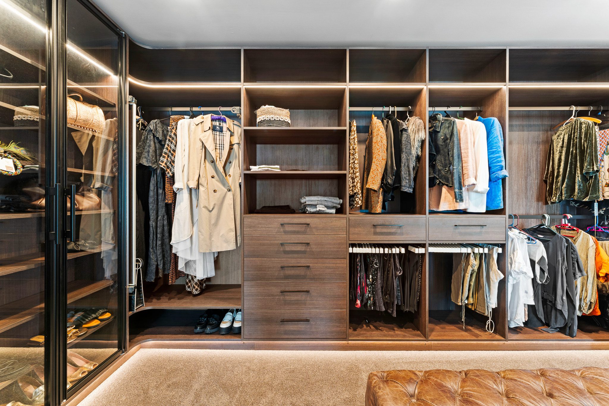 Luxe walk-in wardrobe in dark woodgrain with glass pivot door shoe tower and LED lighting